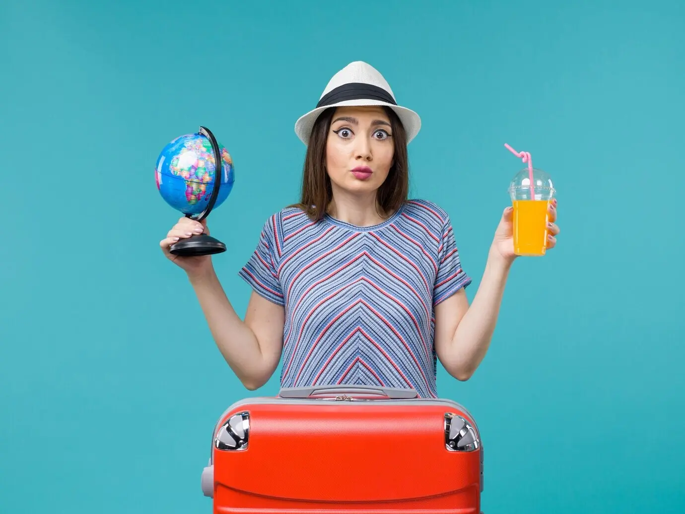 Вид спереди: женщина на отдыхе держит сок и глобус на синем фоне; морское путешествие, летняя поездка, путешествие, отпуск.