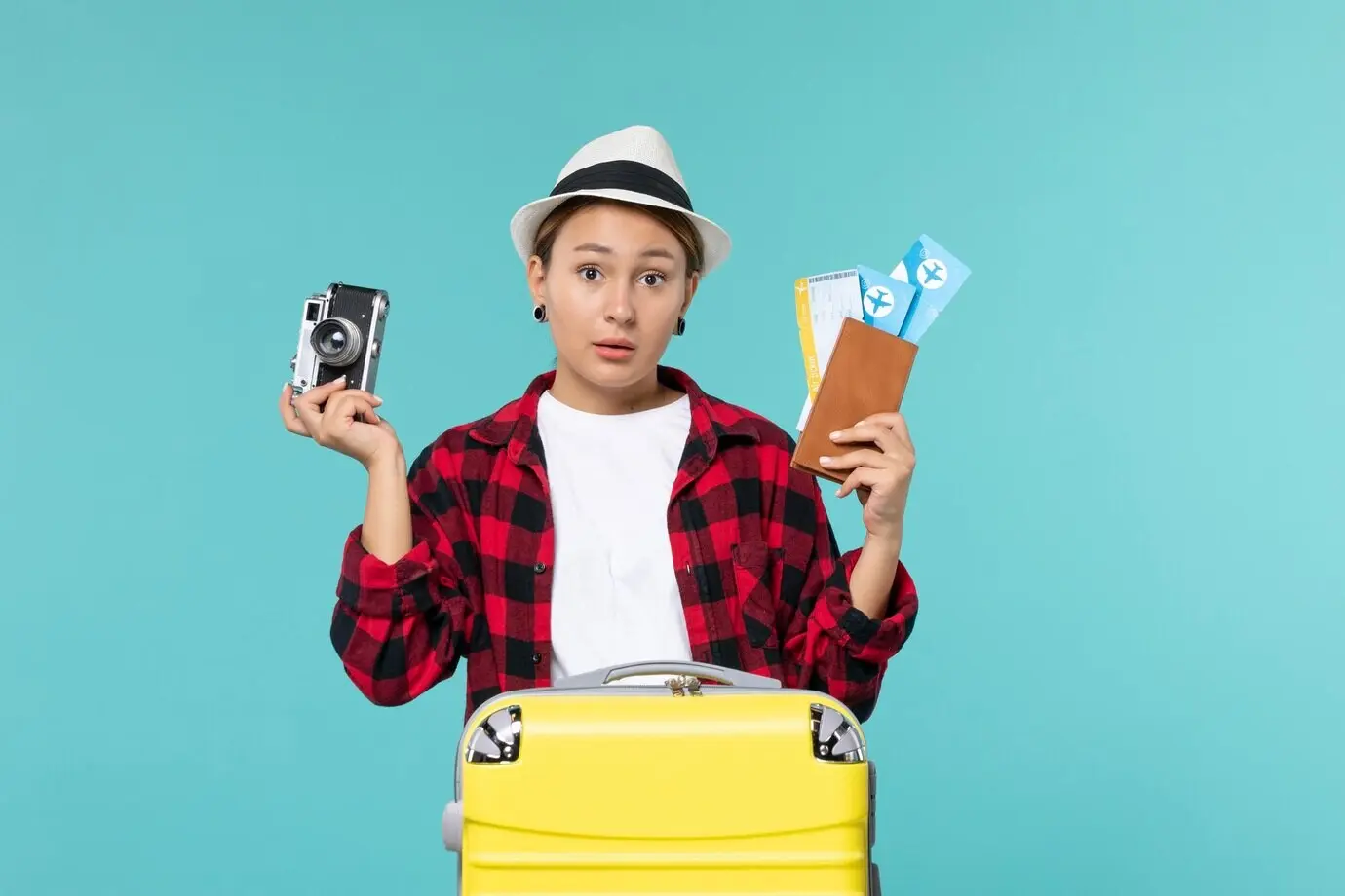 Вид спереди: молодая женщина, отправляющаяся в поездку, держит билеты и камеру на синем фоне.
