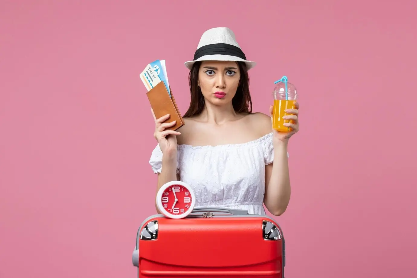 Вид спереди: молодая женщина в отпуске держит билеты и коктейль на фоне розовой стены; женщина, отпуск, путешествие, поездка, летняя жара.